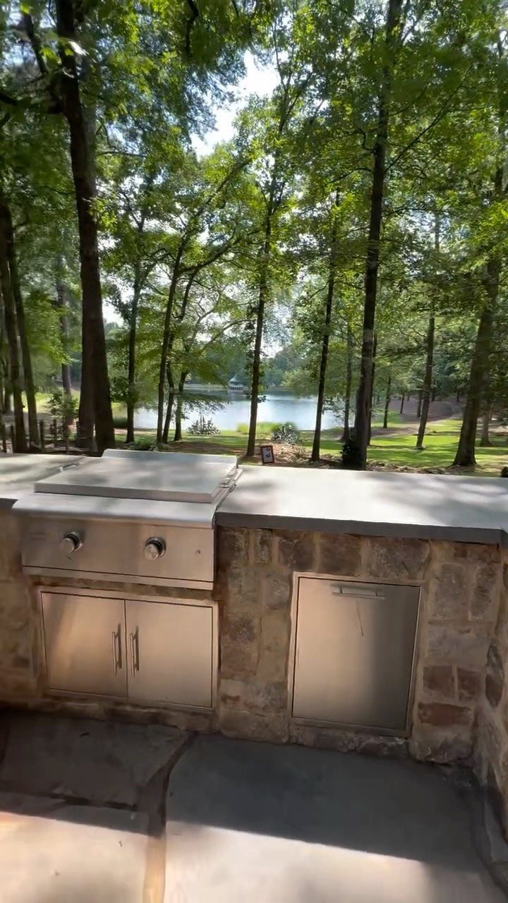 10 Foot Outdoor Kitchen: 5 Plans That Actually Fit the Space 4 Stone outdoor kitchen with stainless steel appliances overlooking a scenic lake through lush green trees.