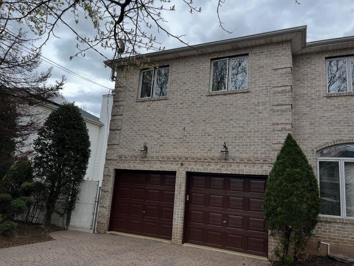 A light grey brick house featuring a two-car garage with dark brown doors and green landscaping.