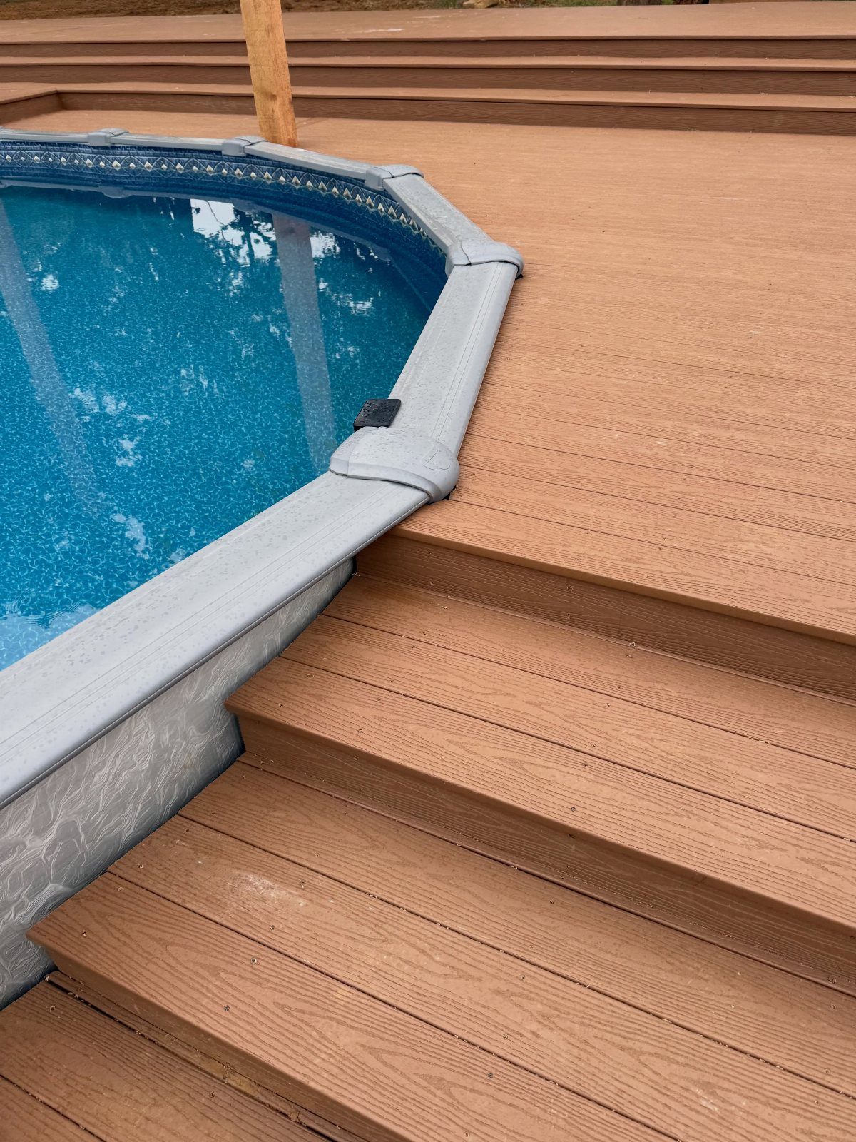 Brown composite decking with wood-grain texture surrounding an above-ground pool with blue water.
