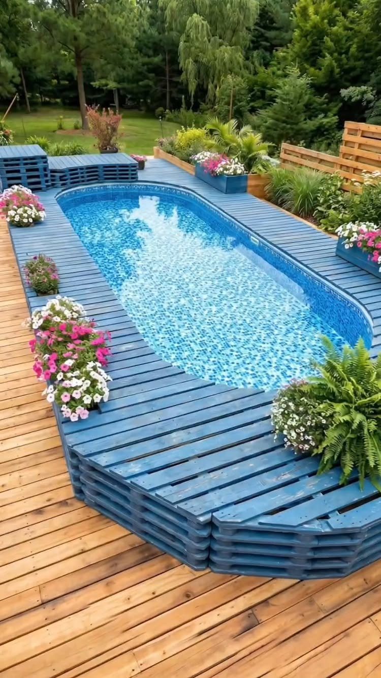 Blue painted wooden pallet deck surrounding an oval above ground pool with colorful flowers.