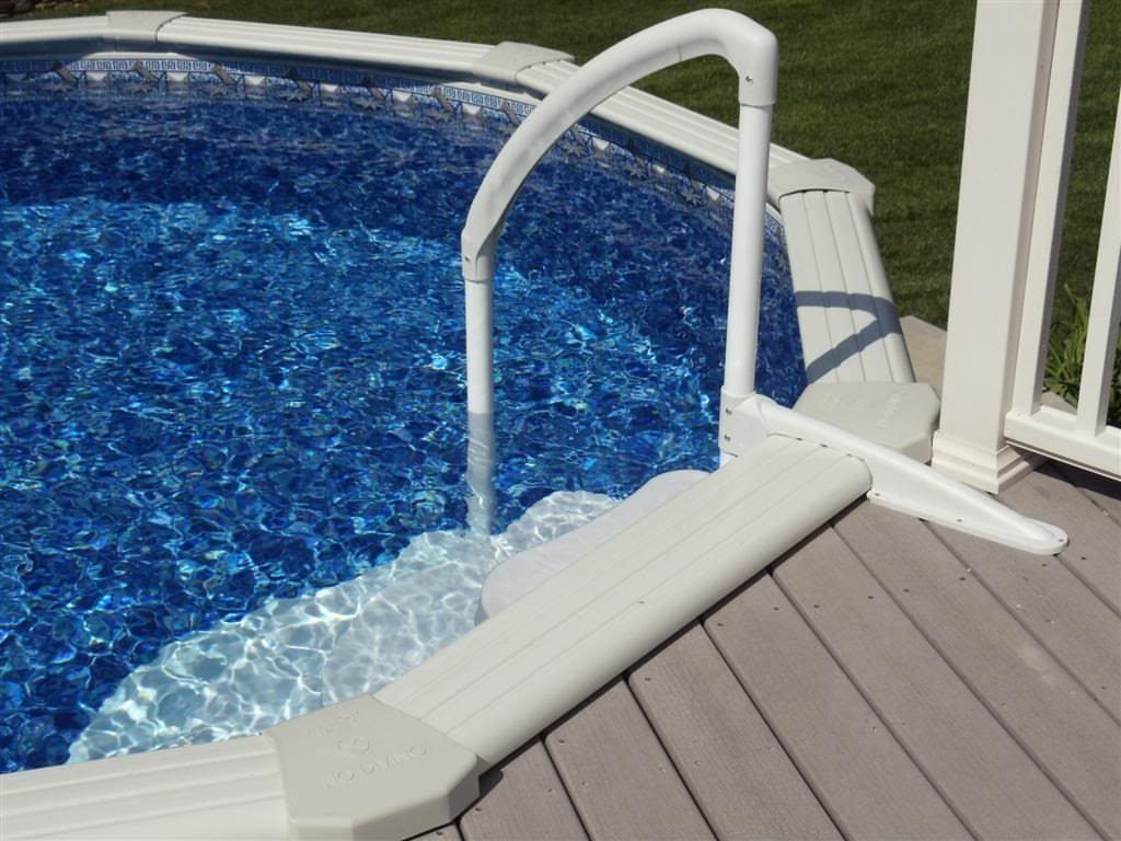 White pool ladder rail extending from a grey deck into clear blue pool water.