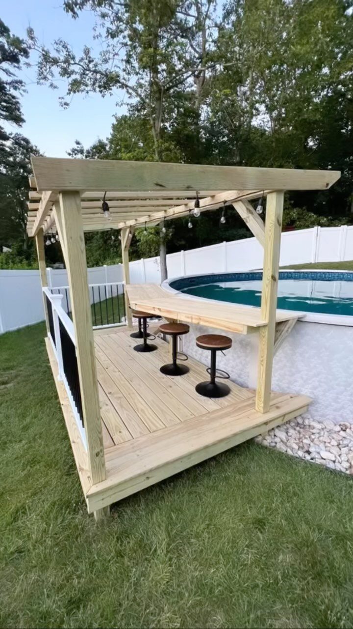 Wooden deck with a built-in bar and pergola next to an above ground pool.