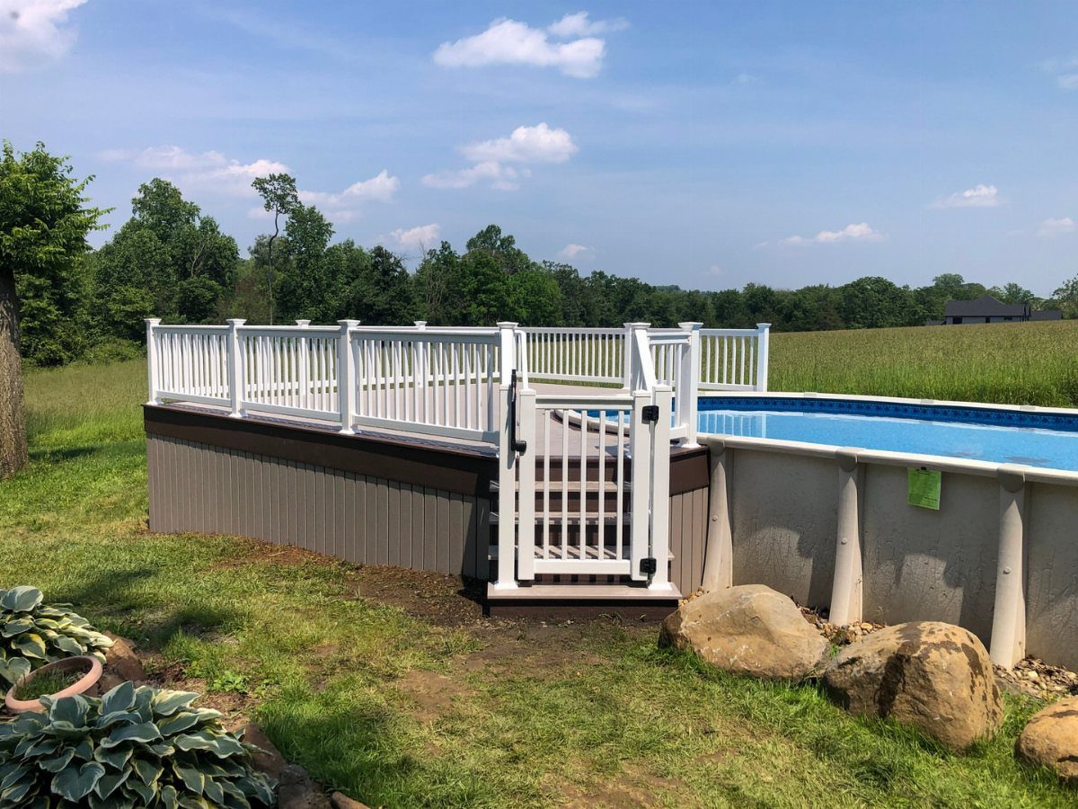 White vinyl safety gate and fence surrounding a wooden deck and above-ground pool.
