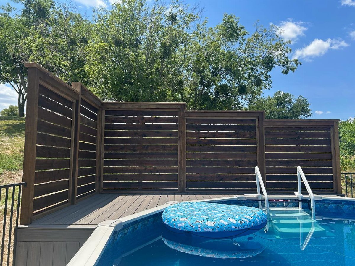 A wooden deck with a slatted privacy screen surrounding a blue above-ground swimming pool.