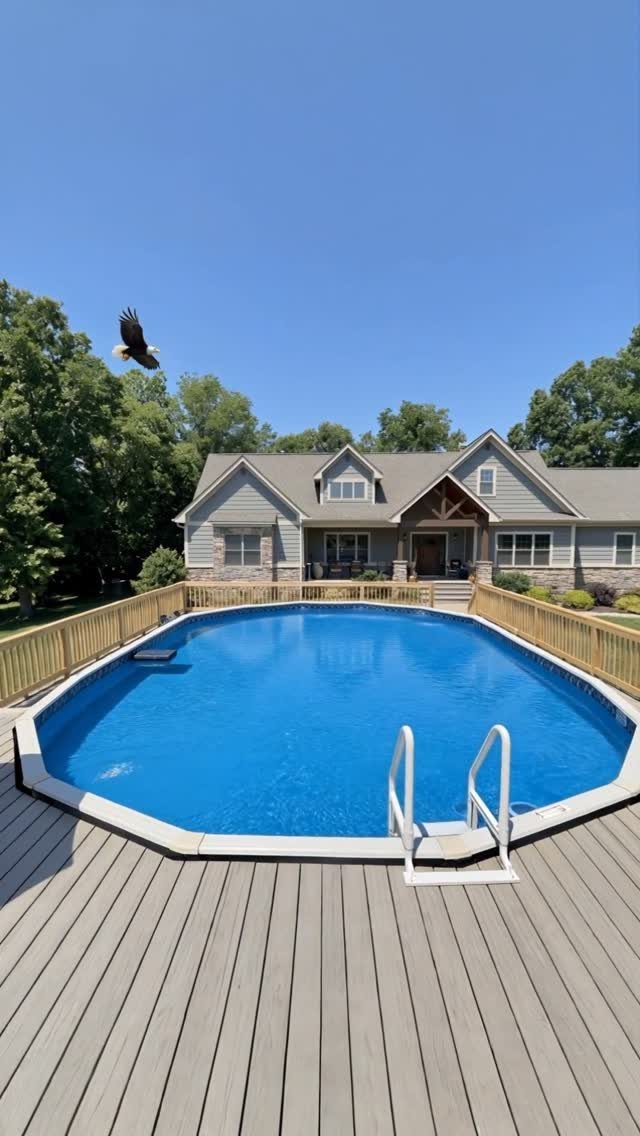 Gray composite deck with light wood railings surrounding a bright blue above ground swimming pool.