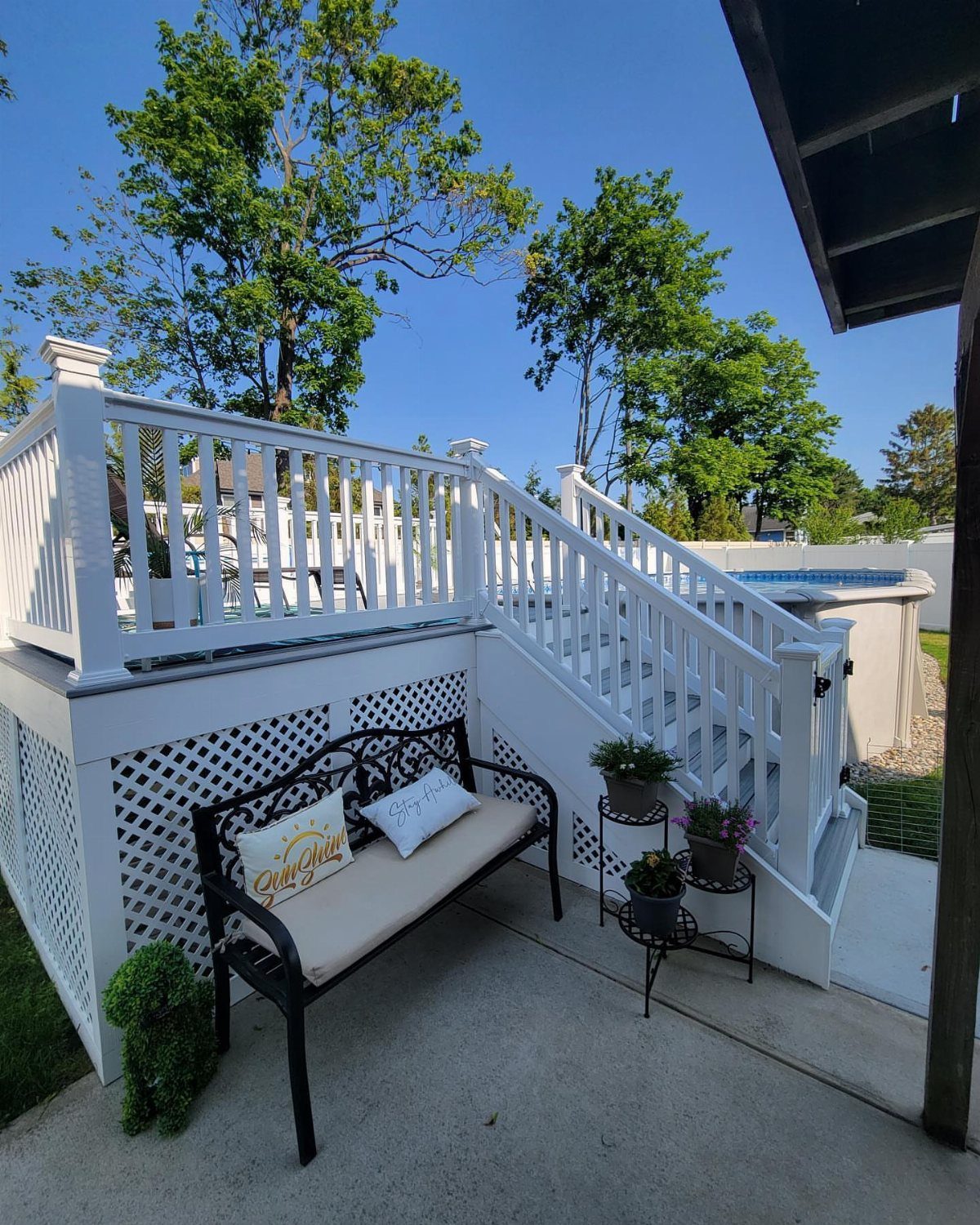 White wooden deck and stairs surrounding an above-ground pool with a bench below.