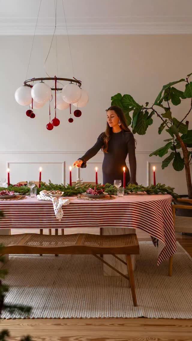 A woman setting a festive dining table with red candles and green garlands.