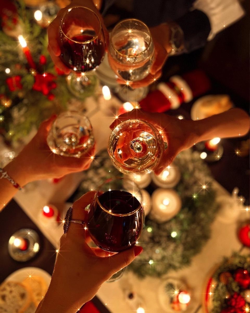 Hands clinking wine glasses in a festive toast over a decorated holiday dinner table.