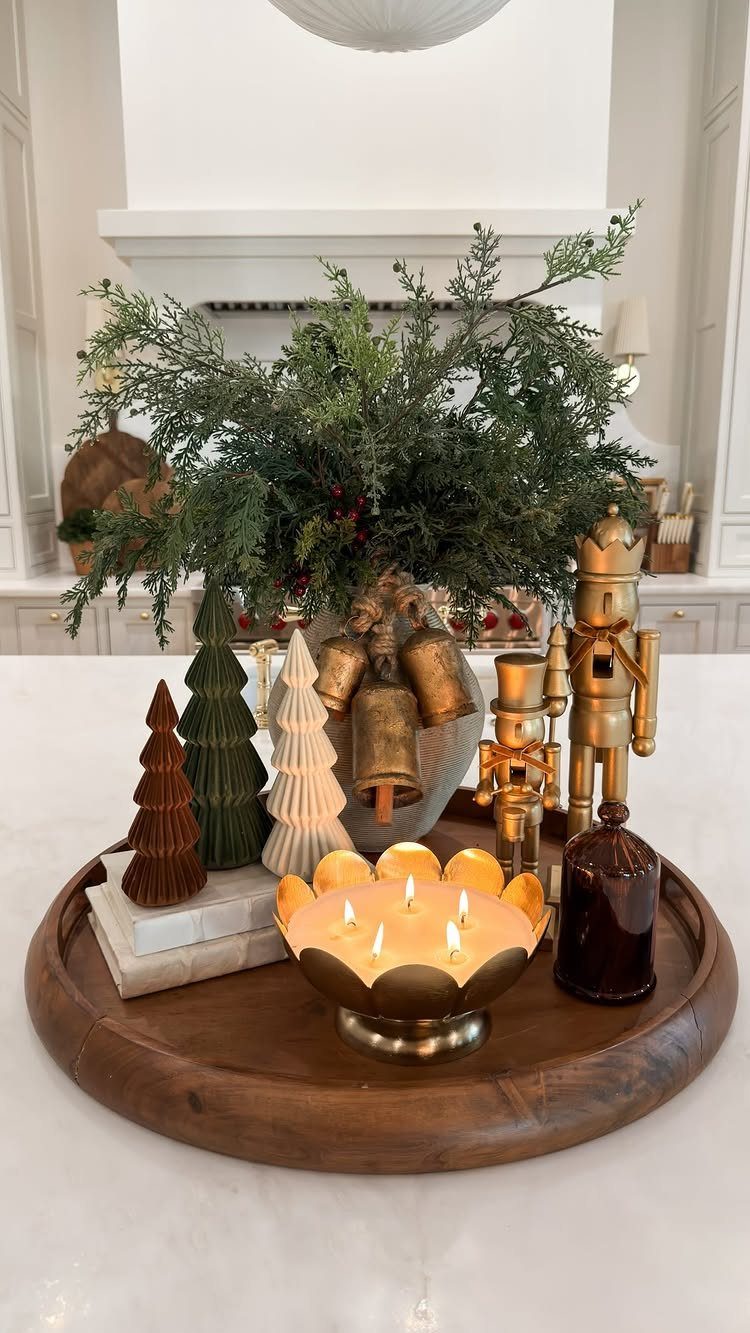 A wooden tray holding decorative Christmas trees, gold bells, a nutcracker, and a lit candle.