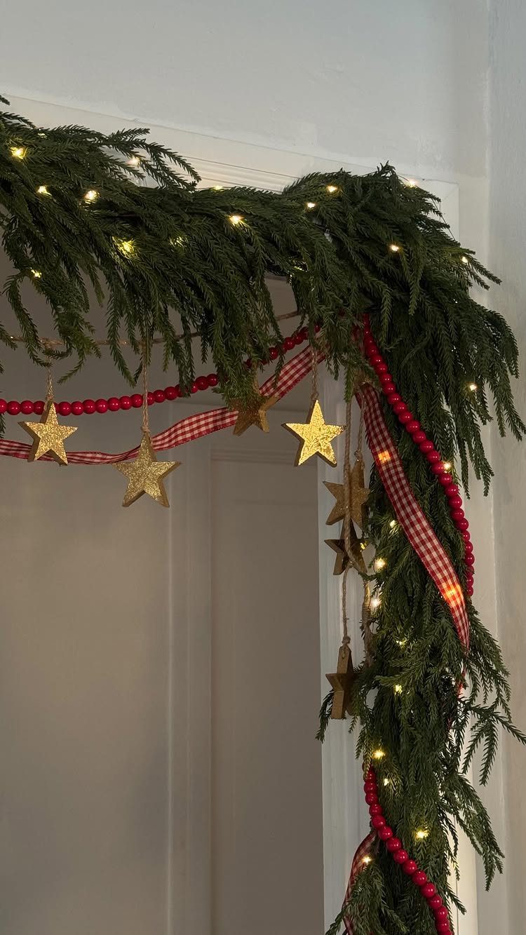 Green evergreen garland with gold stars and red ribbon hanging over a white door frame.