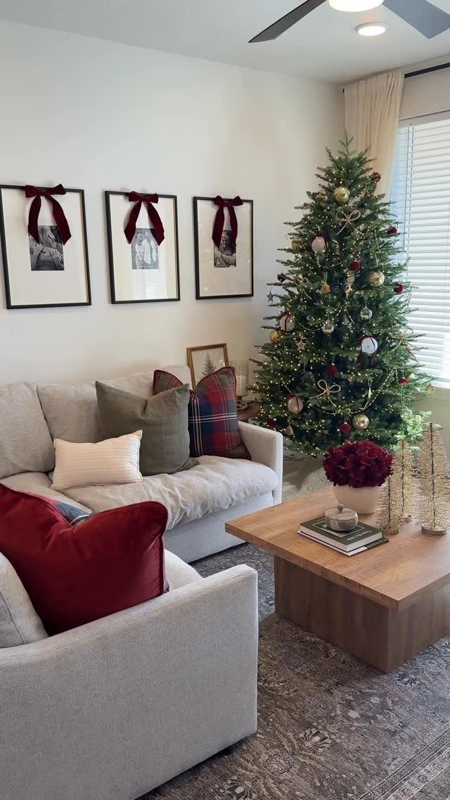 A decorated Christmas tree stands in a living room beside a grey sofa with festive pillows.