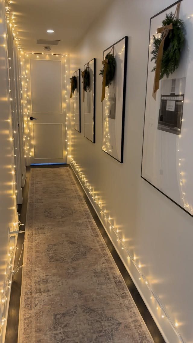 A hallway decorated with warm string lights and small wreaths on framed wall art.