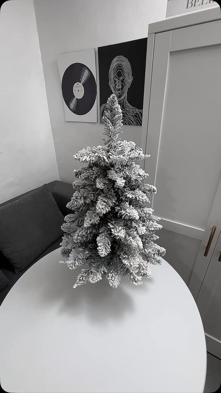 A small flocked white Christmas tree sits on a white table in a modern room.
