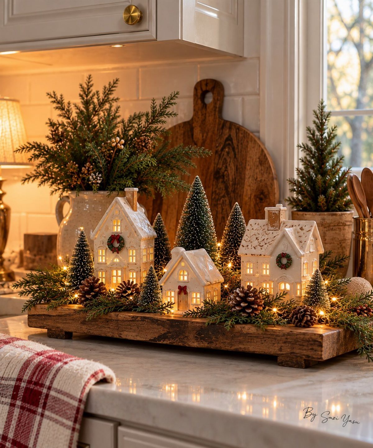 Miniature ceramic houses and evergreen trees arranged with pinecones on a wooden tray.