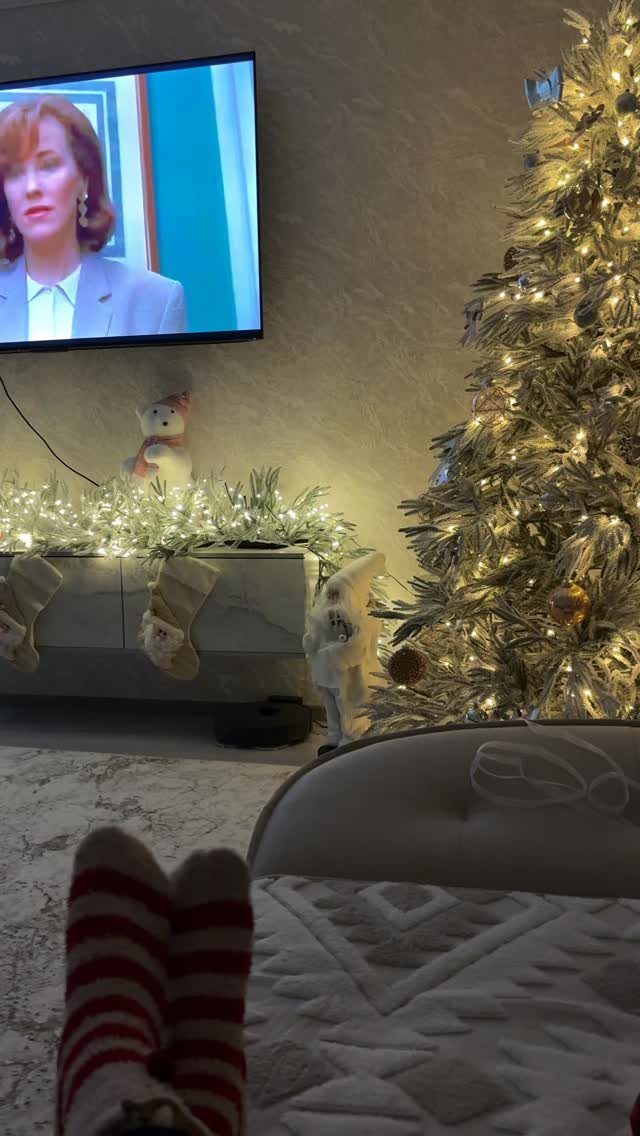 Silver Christmas tree with lights and garland near a television and striped socks.