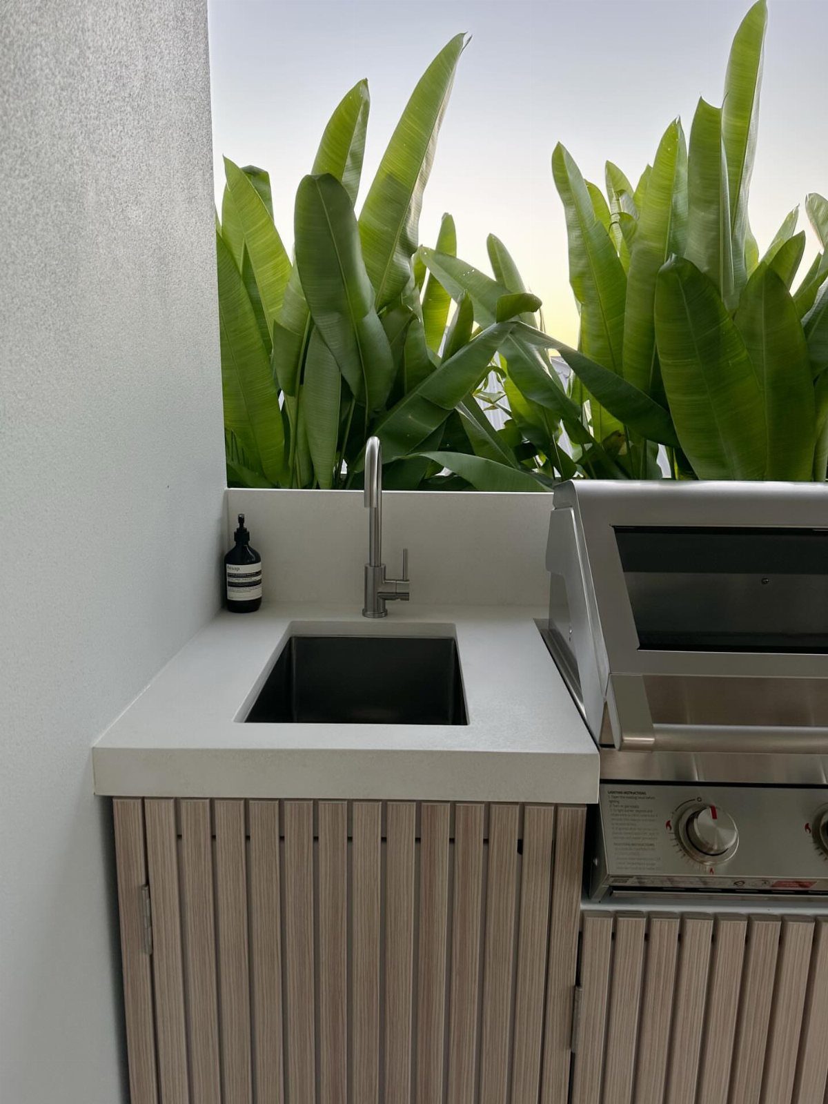 7 Back Porch Outdoor Kitchen Ideas for Covered Cooking 6 A compact outdoor kitchen with a small sink, stainless steel grill, and light grey countertop.