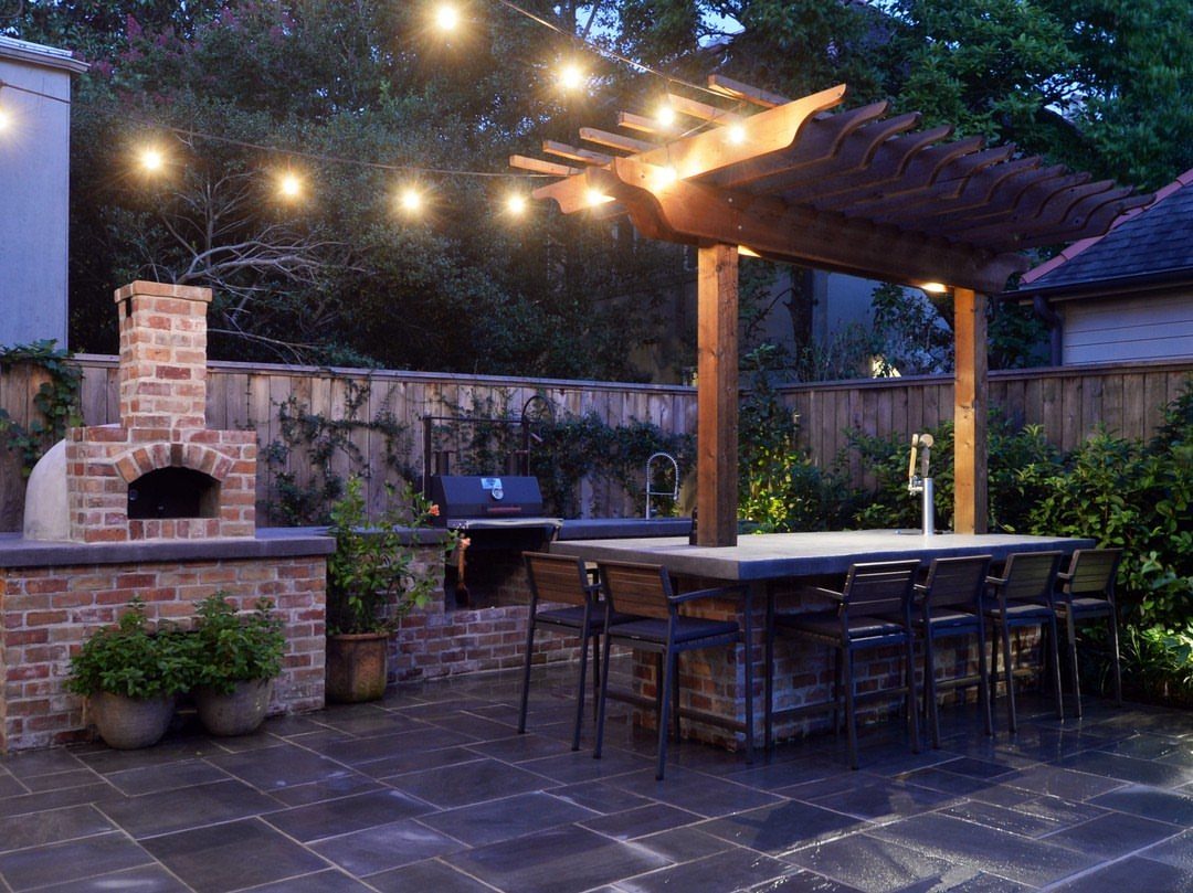 7 Back Porch Outdoor Kitchen Ideas for Covered Cooking 3 Brick outdoor kitchen with a built-in pizza oven, grill, and stone bar under a wooden pergola.