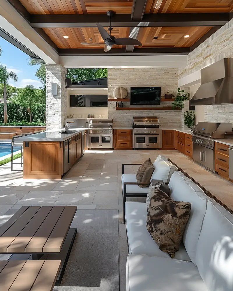 7 Back Porch Outdoor Kitchen Ideas for Covered Cooking 4 Modern outdoor kitchen with stone walls, stainless steel appliances, and wooden cabinetry under a covered patio.