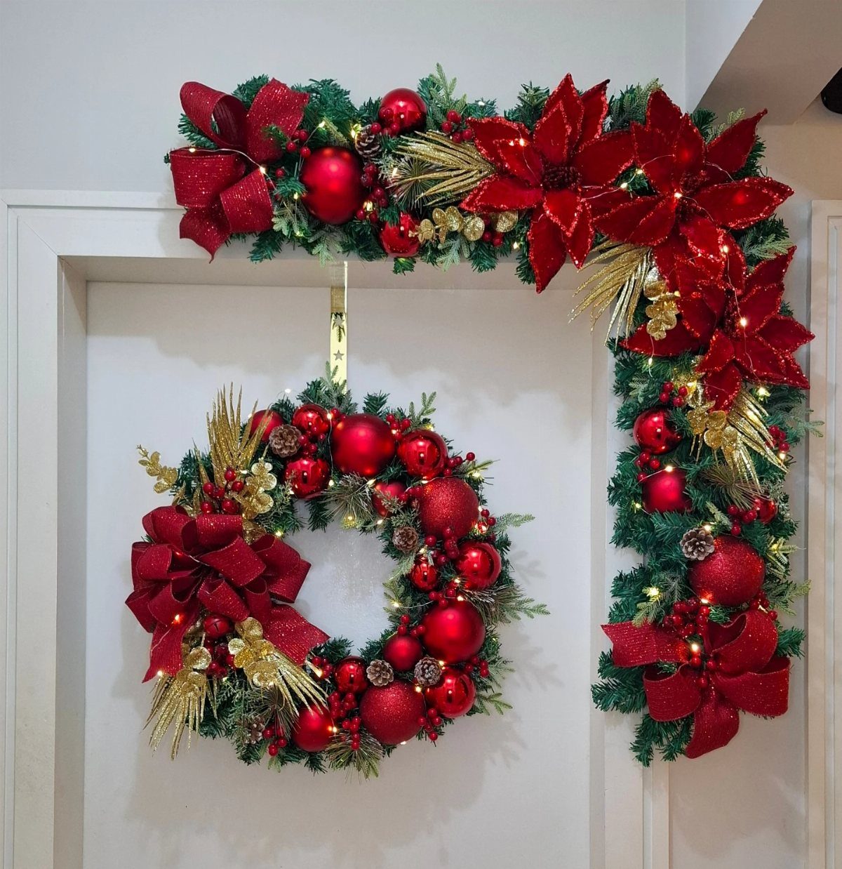 Christmas Bow Decor: 10 Ways to Use Them 4 A red Christmas wreath with a large bow and ornaments hanging on a white door.