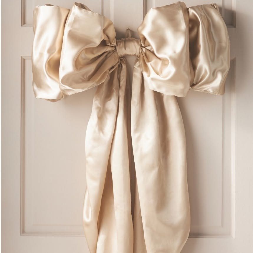 Christmas Bow Decor: 10 Ways to Use Them 8 Large gold satin bow hanging on a white paneled door with long flowing ribbon tails.