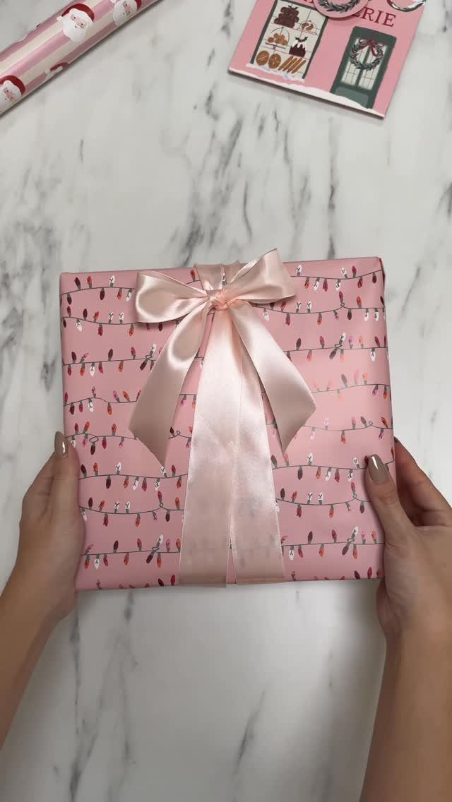 Christmas Bow Decor: 10 Ways to Use Them 9 Hands holding a pink wrapped gift box adorned with a large light pink satin bow.