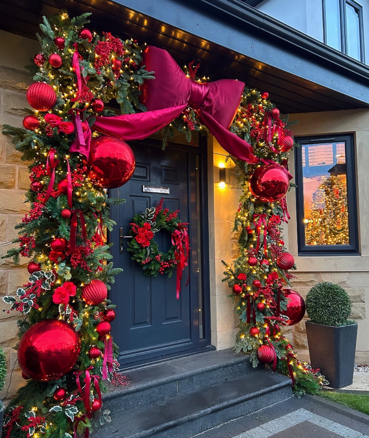 Christmas Bow Decor: 10 Ways to Use Them 5 Evergreen garland with red ornaments and a large magenta bow decorating a house entrance.