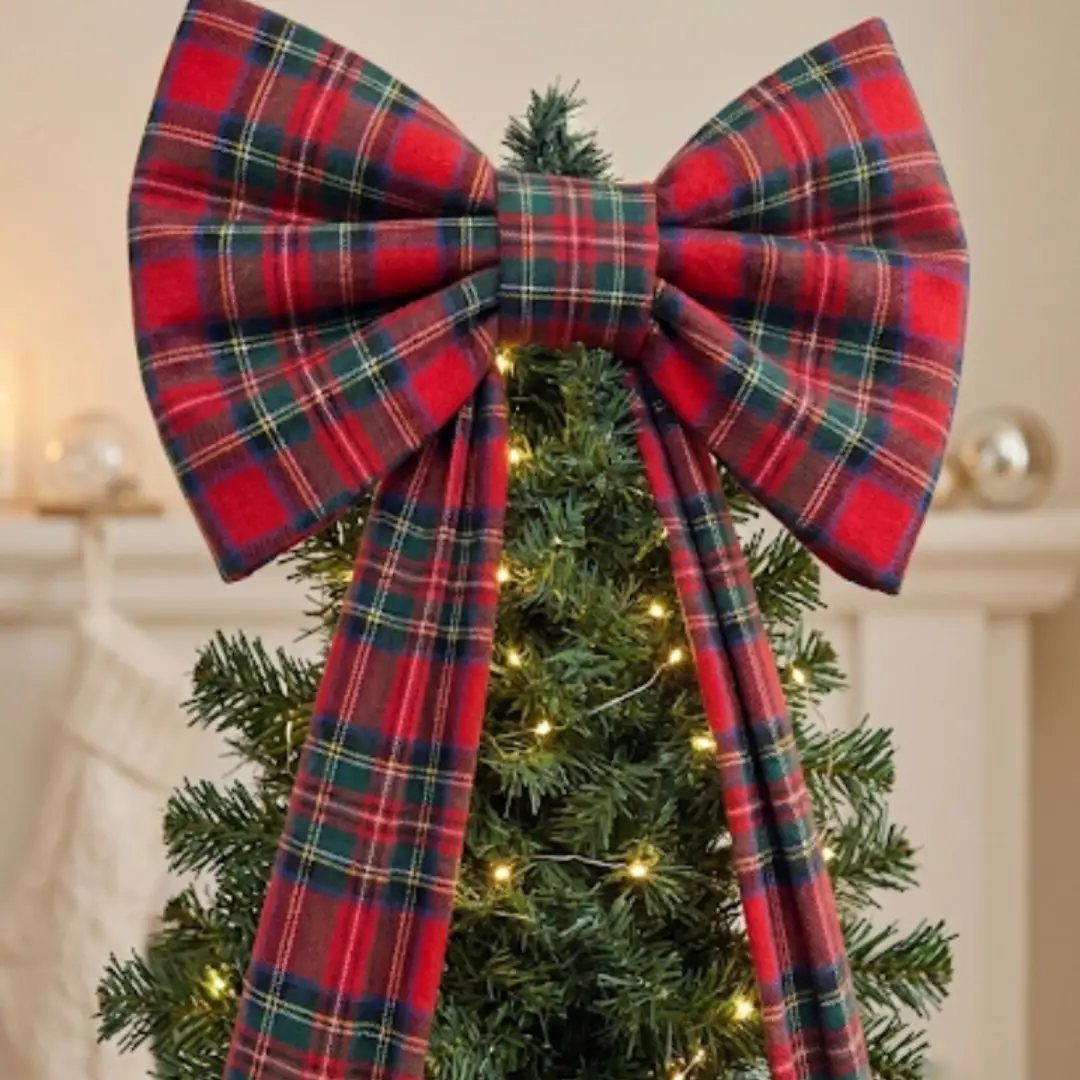Christmas Bow Decor: 10 Ways to Use Them 7 A large red and green plaid fabric bow decorating the top of a lit Christmas tree.