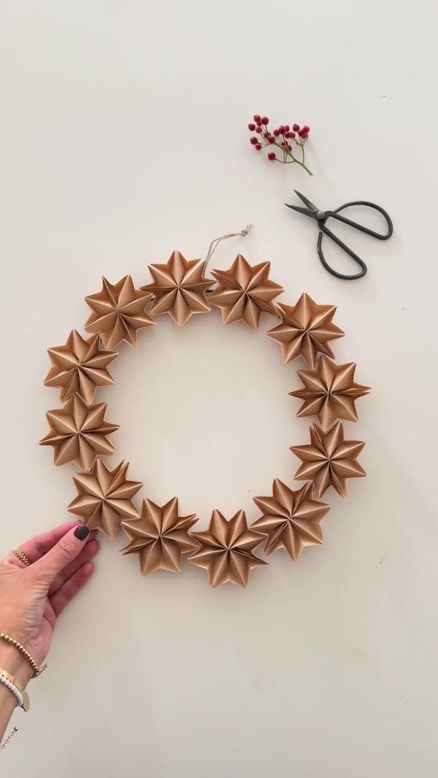 A gold paper star wreath lies on a white surface next to scissors and red berries.
