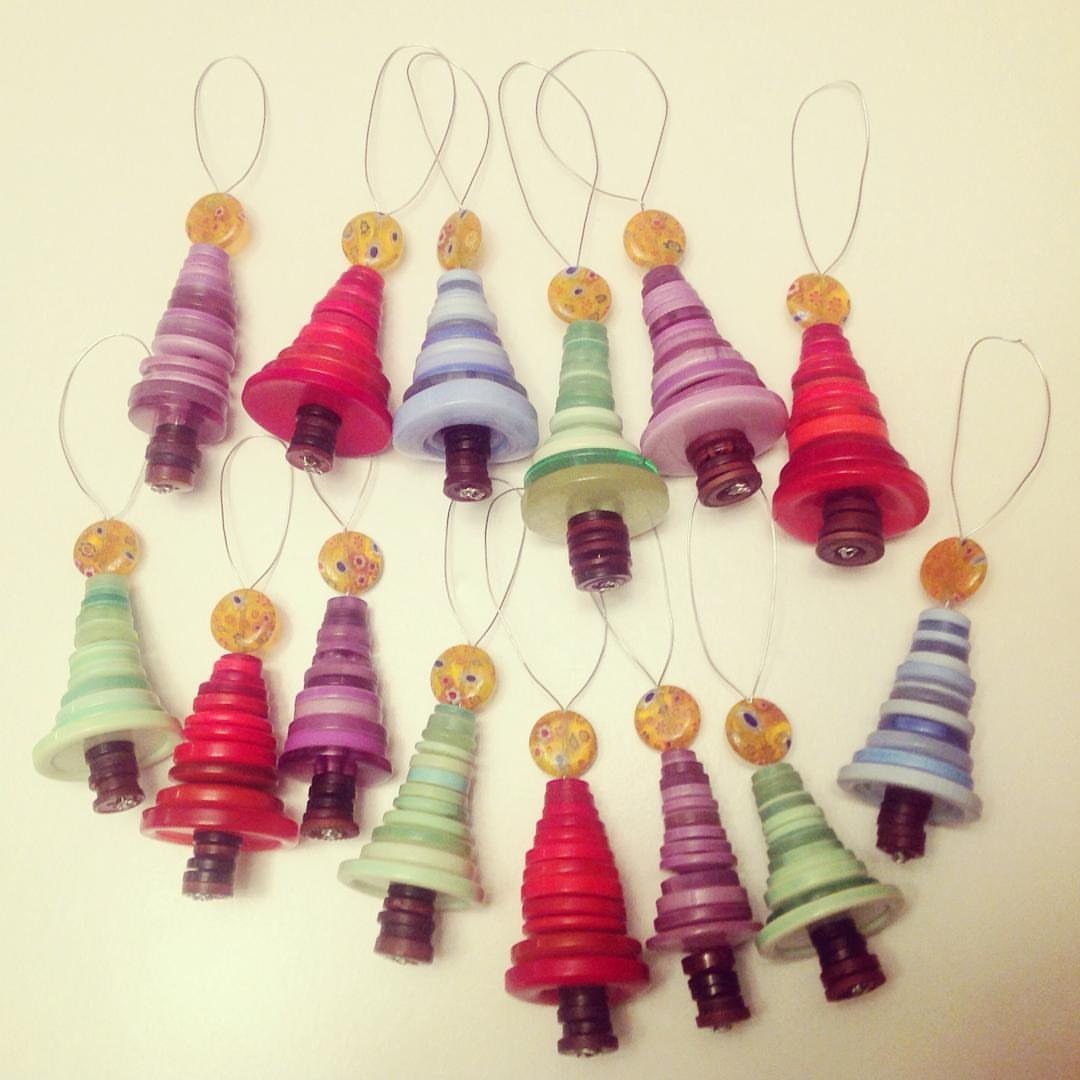 Several colorful button Christmas tree ornaments in pink, blue, and green stacked on a white surface.