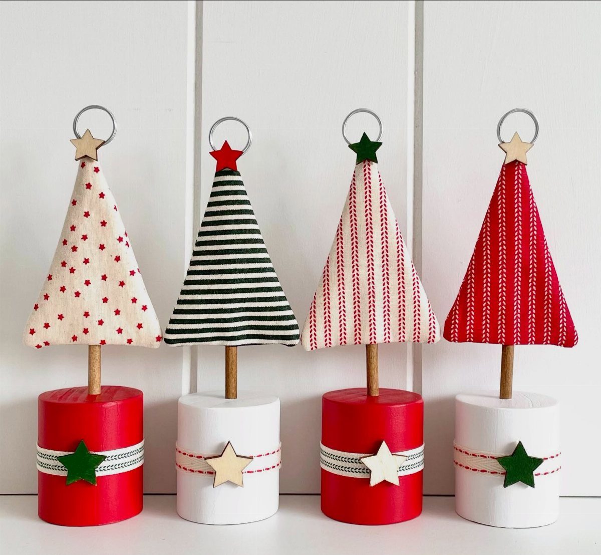Four fabric Christmas tree place card holders with patterned designs on painted wooden bases.