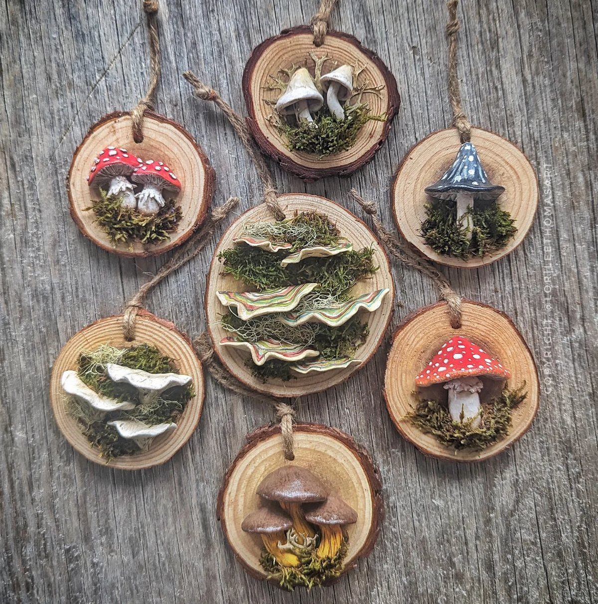Handmade clay mushroom ornaments resting on wood slices with moss and twine hangers.