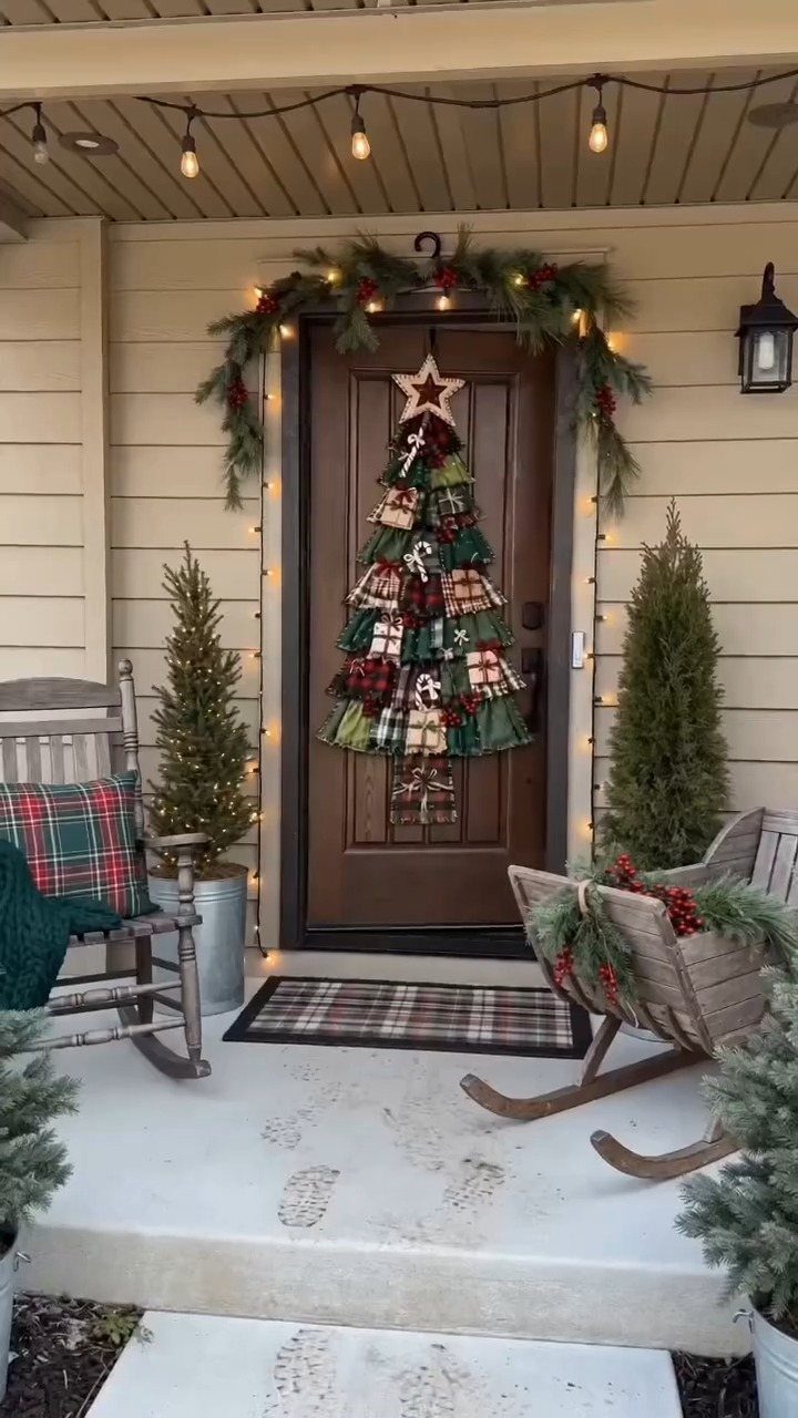Fabric Christmas tree ornament hanging on a dark brown front door decorated with festive greenery.