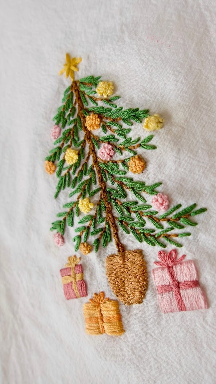 Embroidered Christmas tree with colorful ornaments and small gift boxes on white fabric.