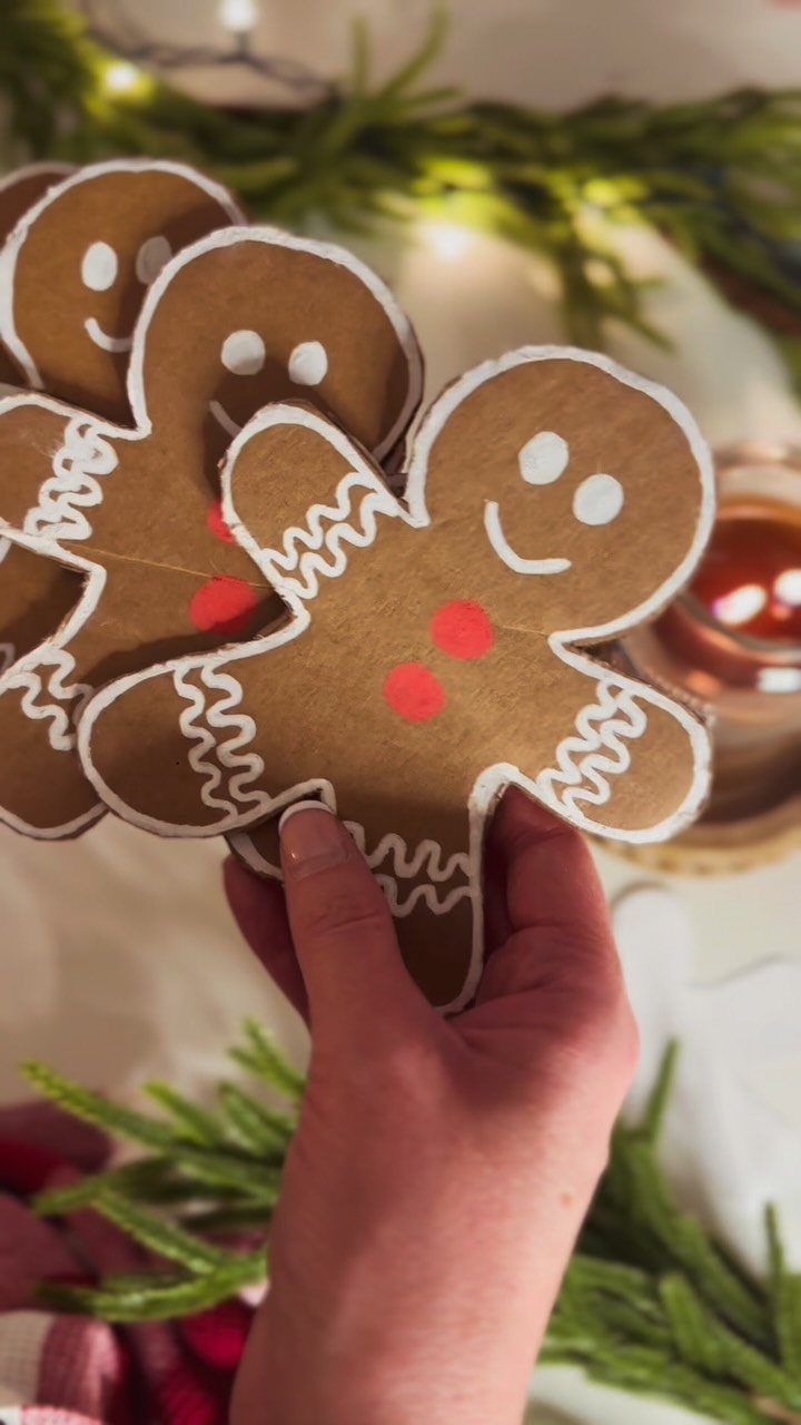 Hand holding several brown cardboard gingerbread man ornaments with white decorative outlines.