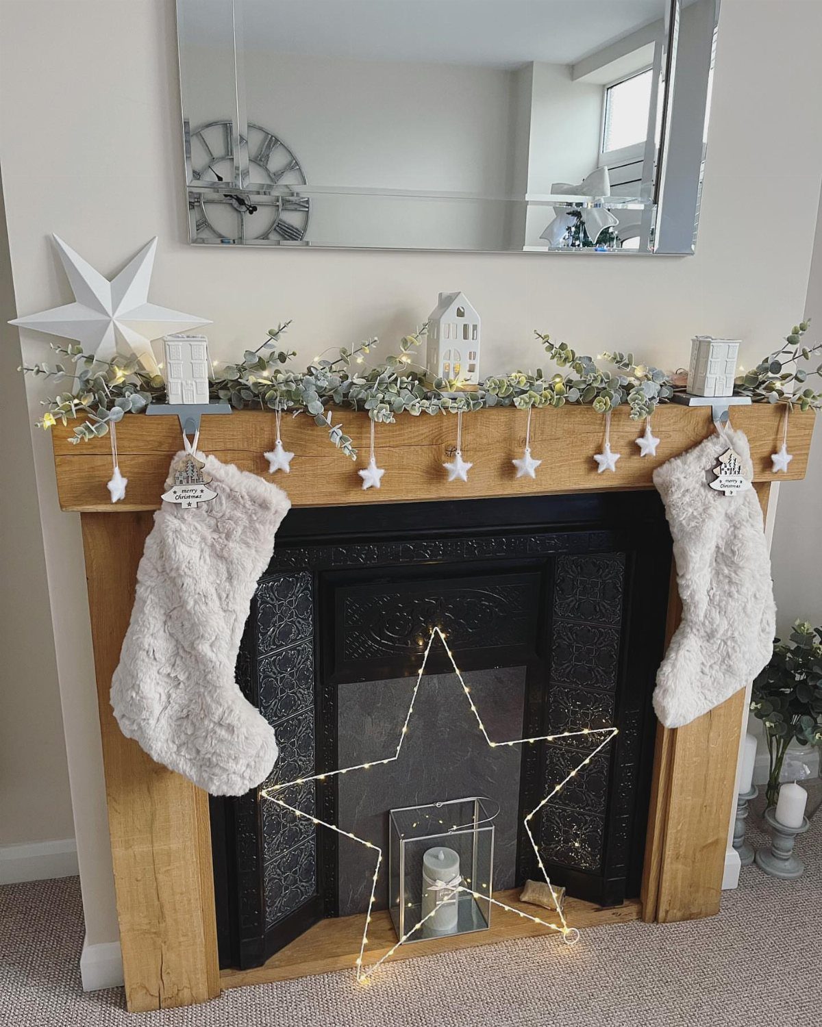 Wooden fireplace mantel decorated with white stars, green garland, and fuzzy white stockings.