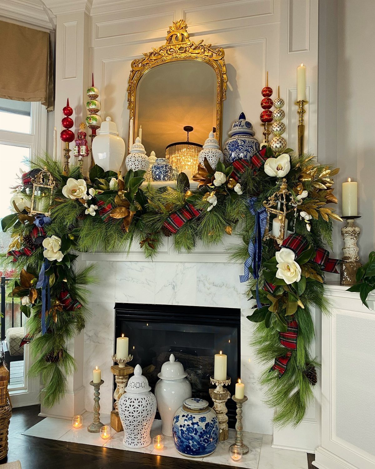 Evergreen garland with white flowers and red plaid ribbons decorating a white marble fireplace mantel.