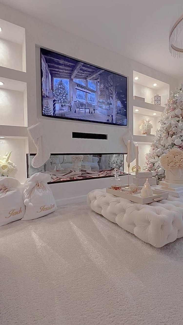 White living room with a modern fireplace, flocked Christmas tree, and tufted ottoman.