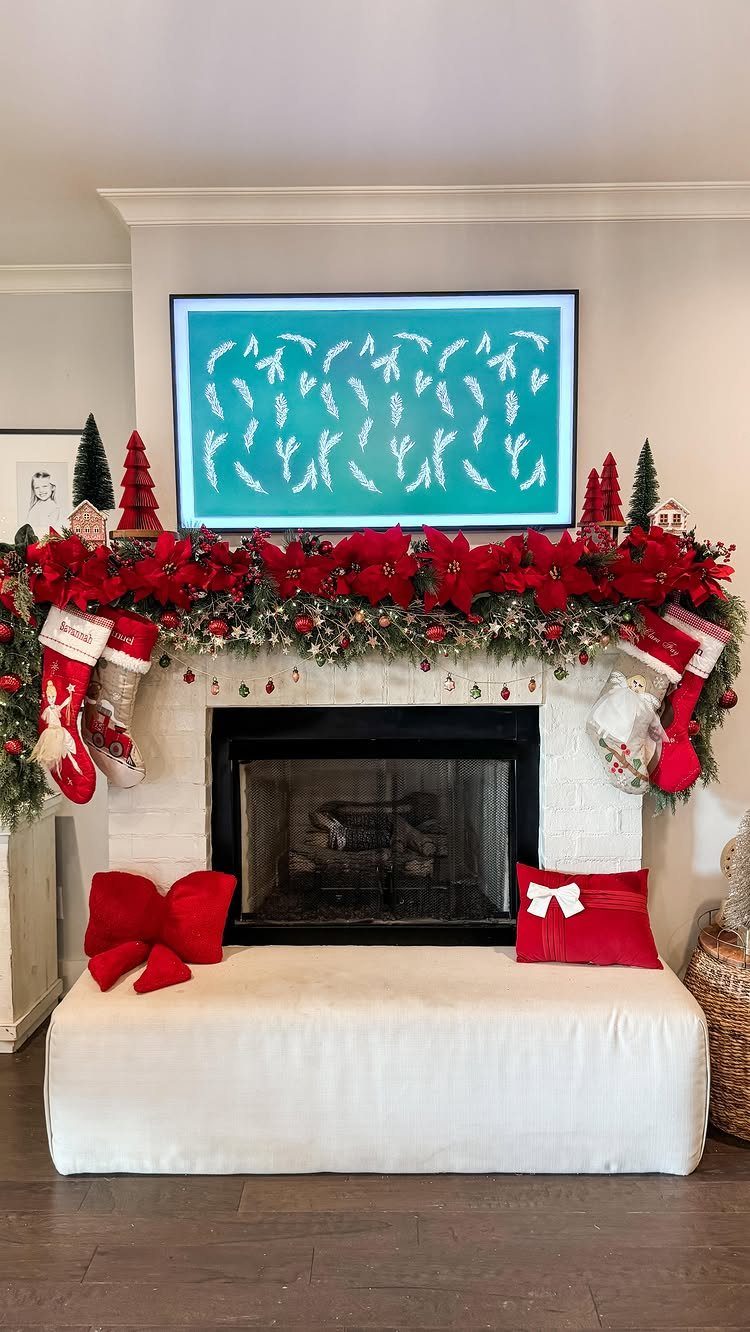 Decorated white fireplace mantel with red poinsettias, green garland, and hanging red stockings.