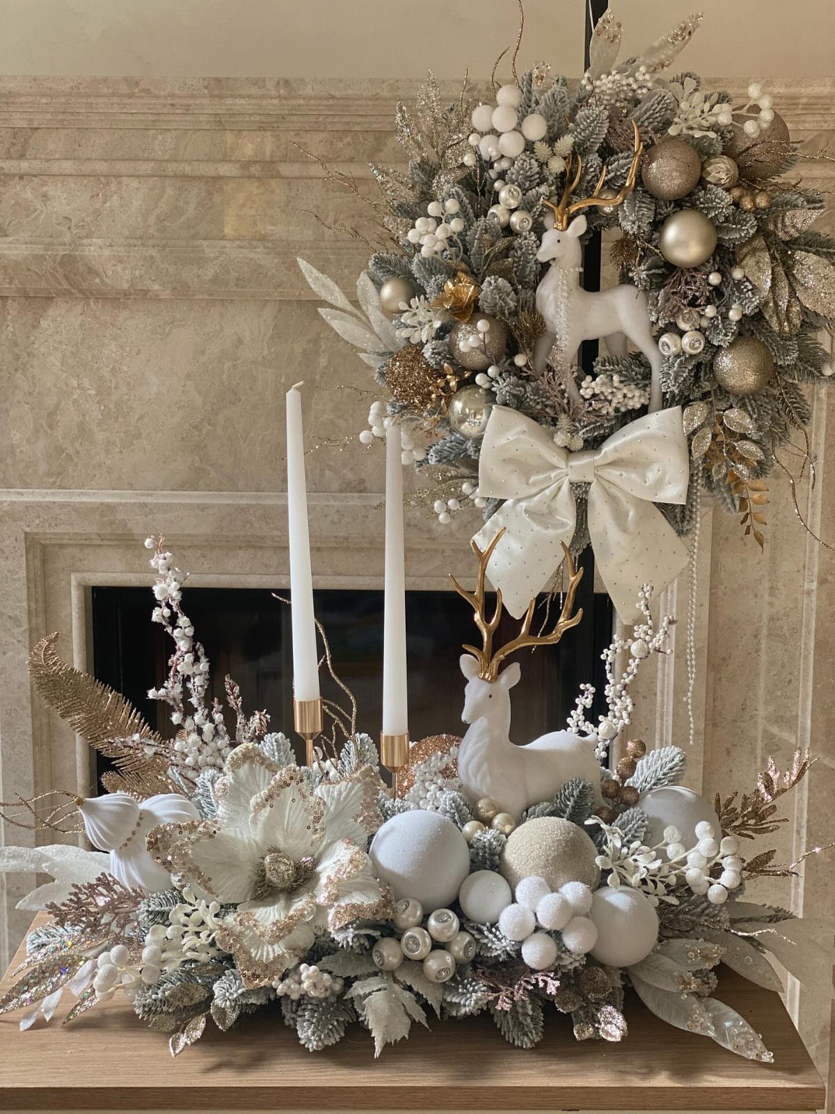 White and gold Christmas decorations including reindeer, candles, and ornaments on a fireplace mantel.