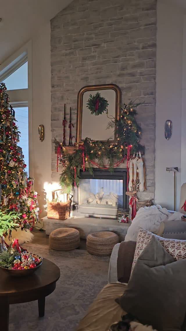 A stone fireplace decorated with green garland, red ribbons, white stockings, and a gold mirror.