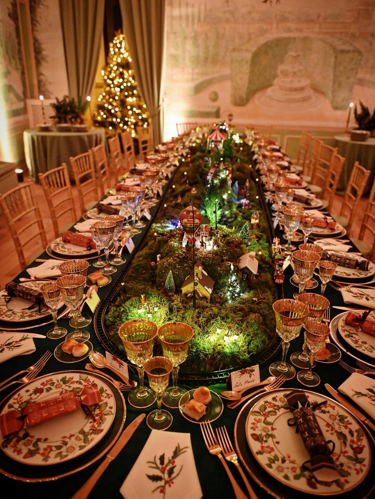 Christmas Table Centerpieces: 8 Ideas for Holiday Tables 2 A long festive dining table featuring a mossy centerpiece with miniature houses and glowing lights.