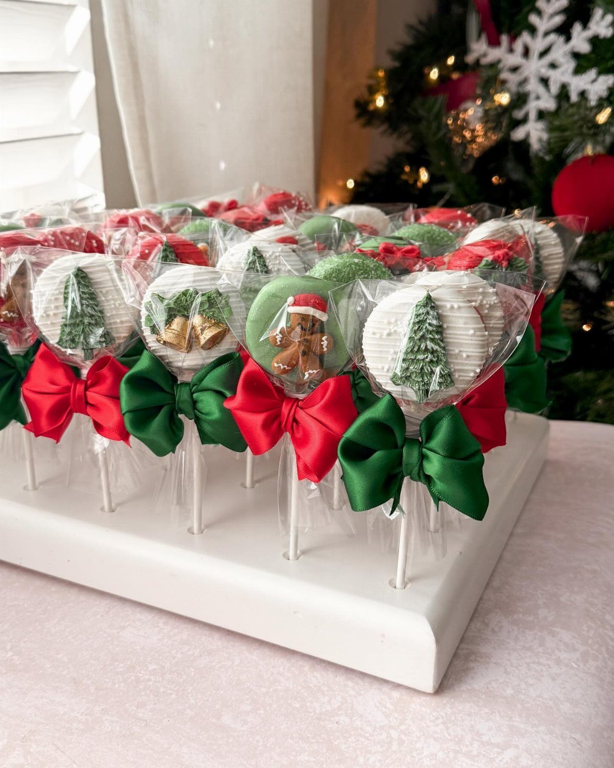 Decorated Christmas tree cookie pops with red and green bows arranged on a white display stand.