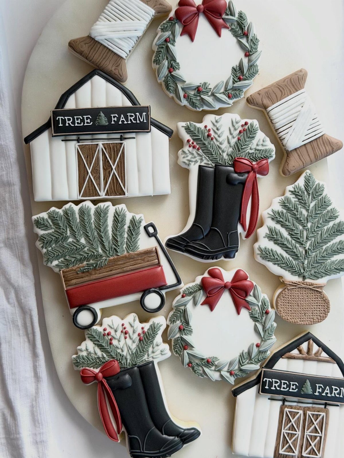 Decorated sugar cookies shaped like barns, boots, wreaths, and a pine tree on a white plate.
