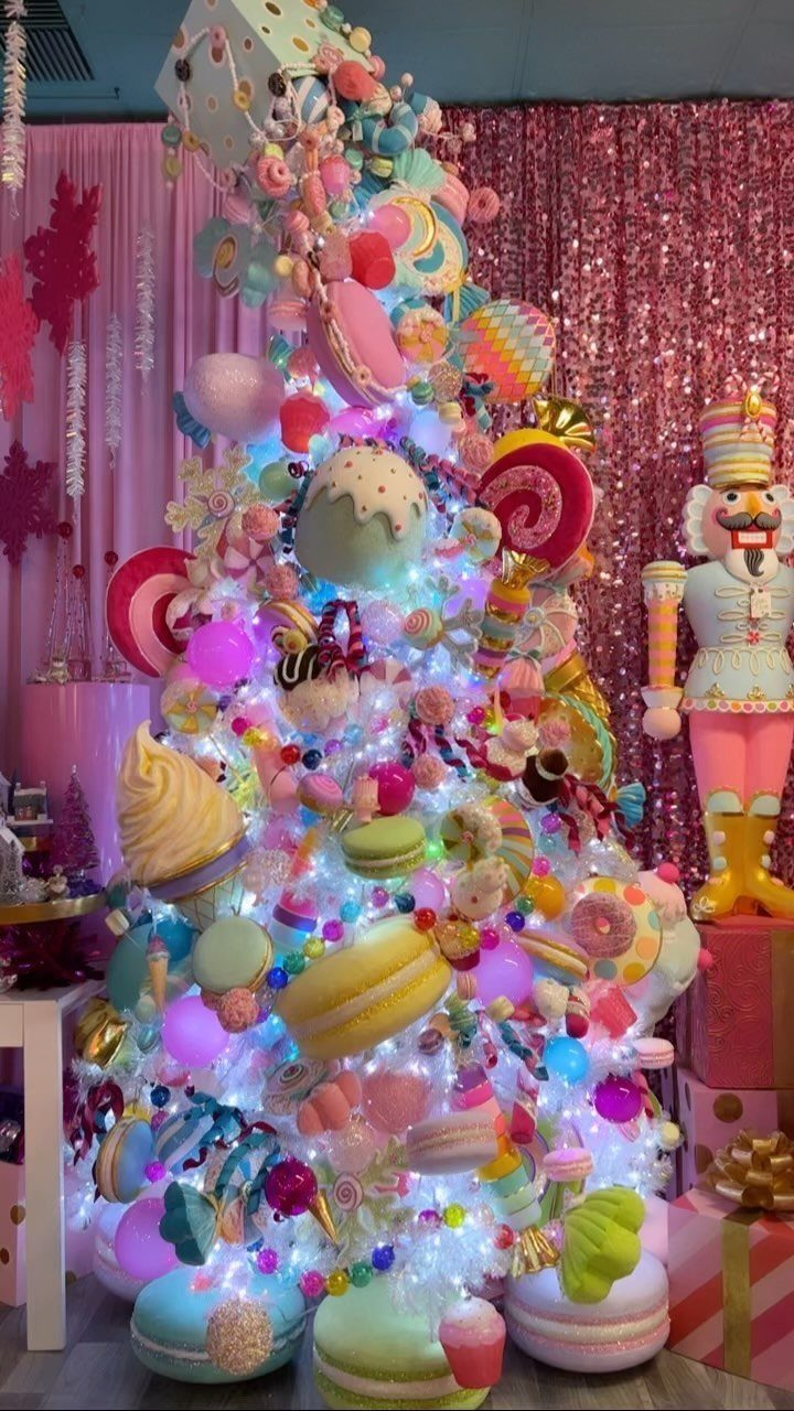 A Christmas tree decorated with large pastel macarons and colorful candy ornaments against pink sequins.