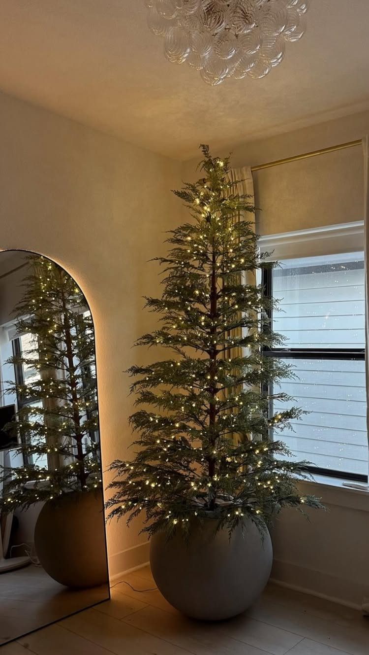 A minimalist evergreen tree decorated with warm white lights in a large grey pot.