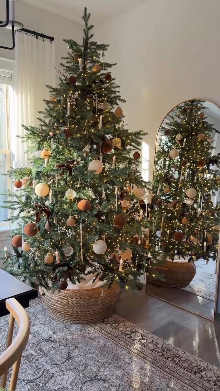 A decorated green Christmas tree with warm lights and neutral ornaments in a woven basket.
