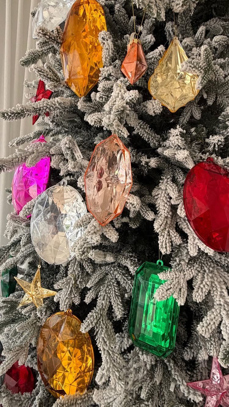 Large faceted jewel-shaped ornaments in various colors hanging on a flocked Christmas tree.
