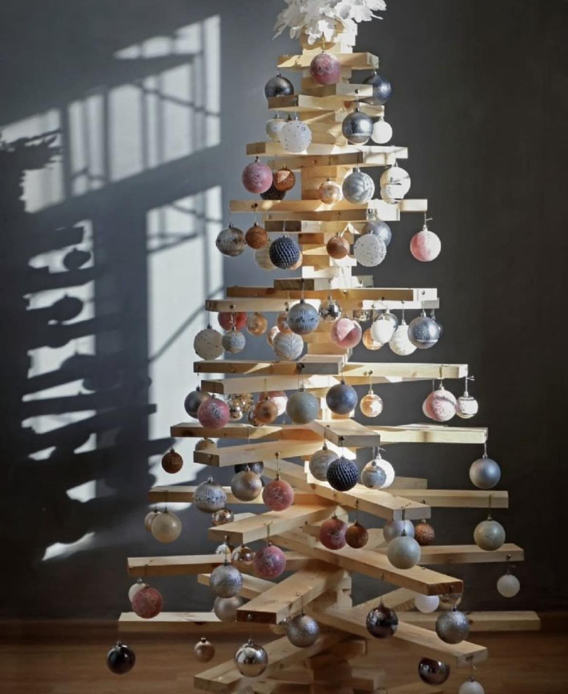 A Christmas tree made of stacked wooden planks decorated with colorful round ornaments.