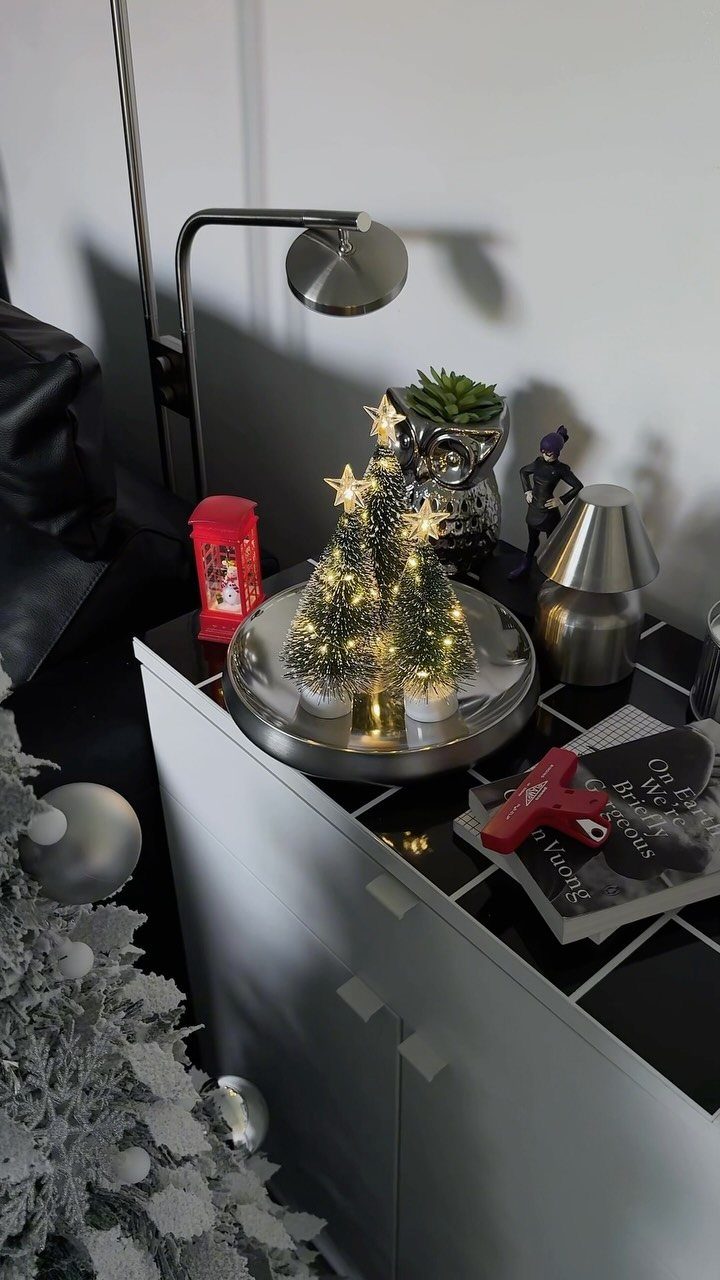 Three miniature lighted Christmas trees with gold stars sitting on a silver tray.