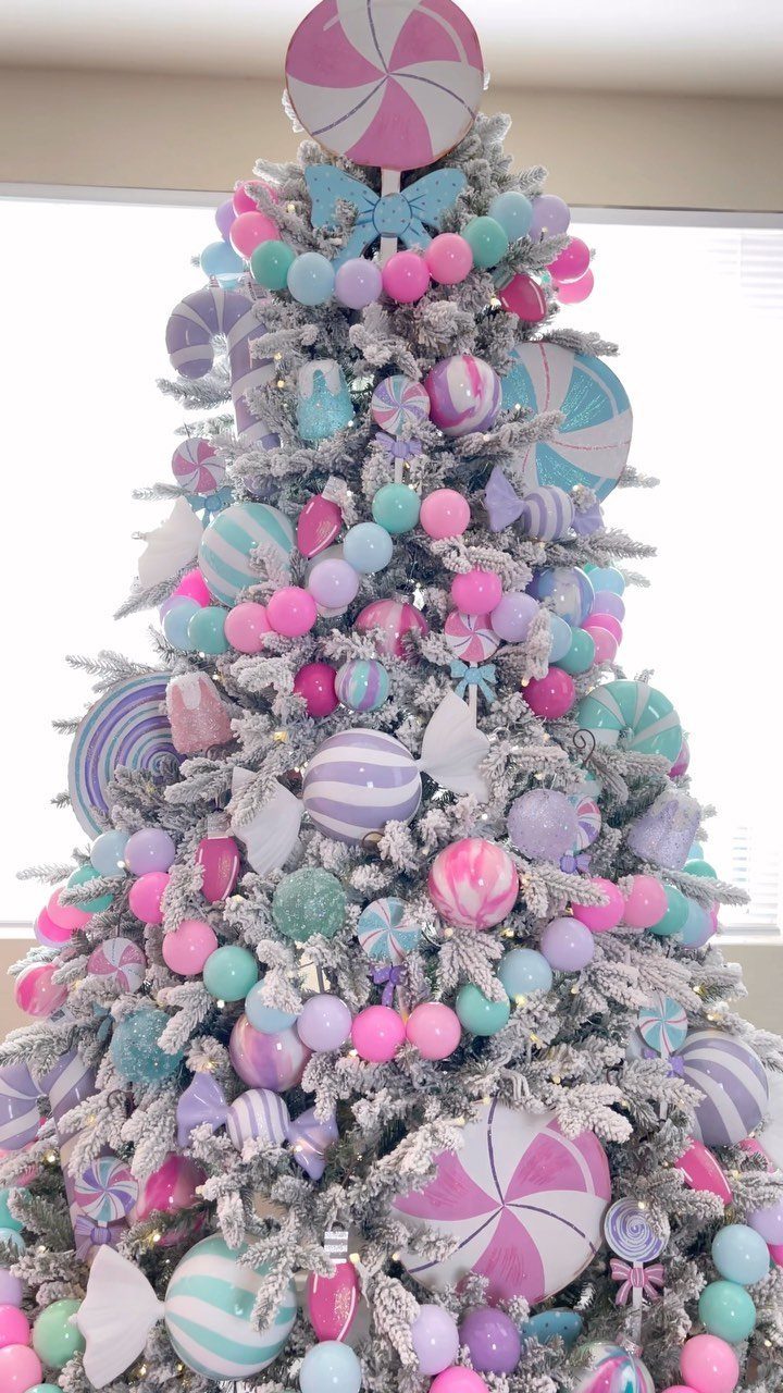 A white flocked Christmas tree decorated with pastel pink, mint, and lavender candy-themed ornaments.